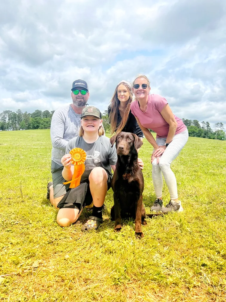 A family poses for a picture with a dog in a field.