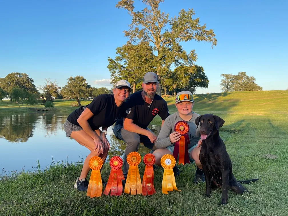 three people holding multiple ribbons and posing next to their dog