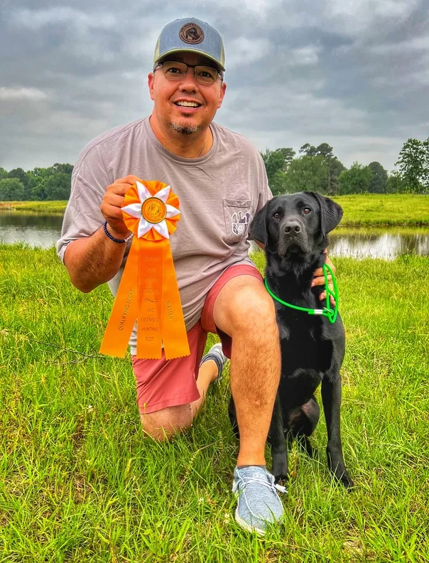 man holds orange ribbon and kneels next to his dog