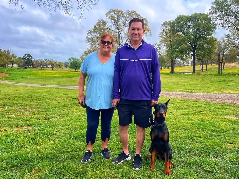 couple standing in a field next to their dog