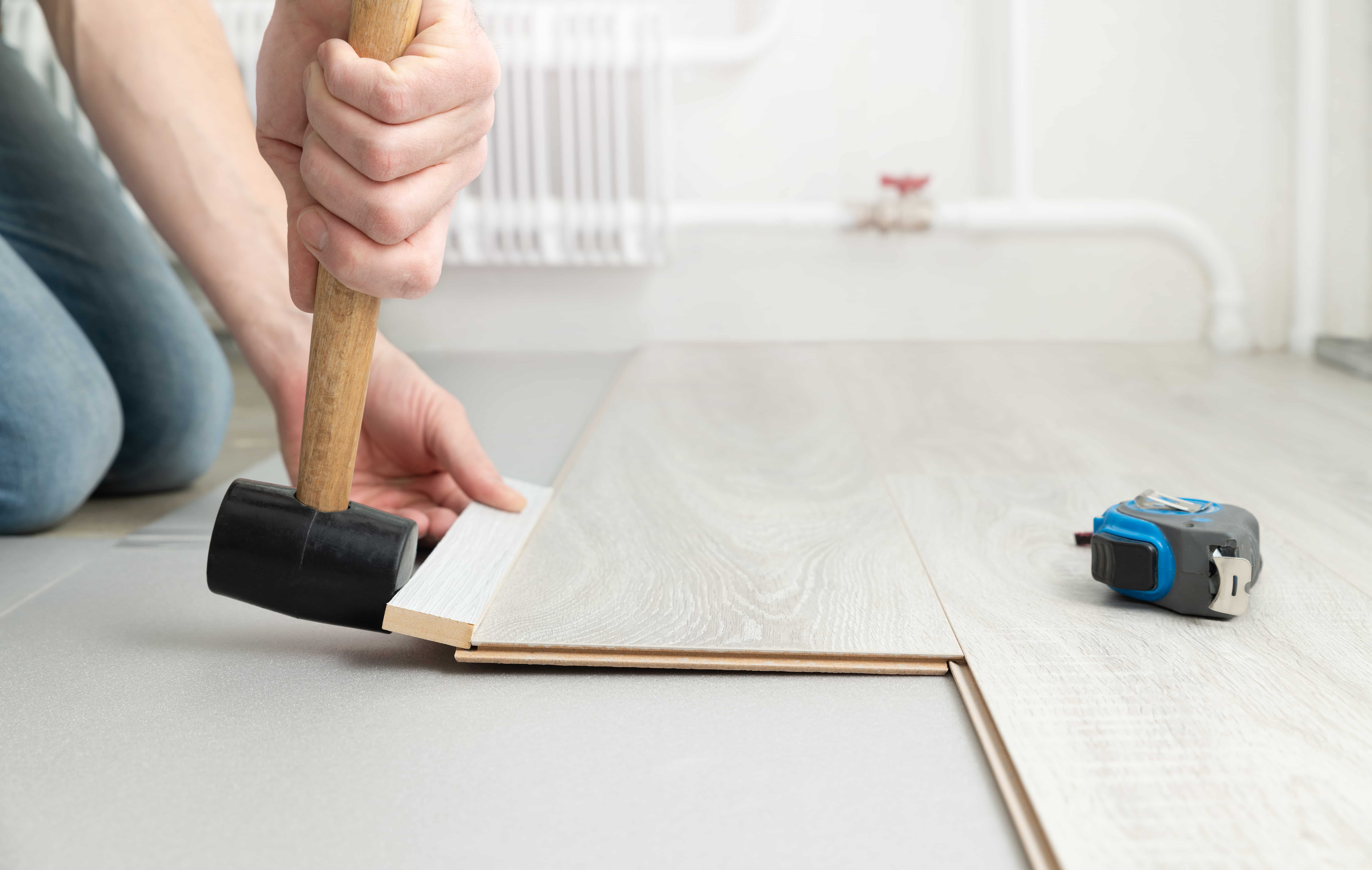 Laminate flooring being installed over concrete. The installer gently taps the edge of a board with a mallet against a piece of wood to click it into place.