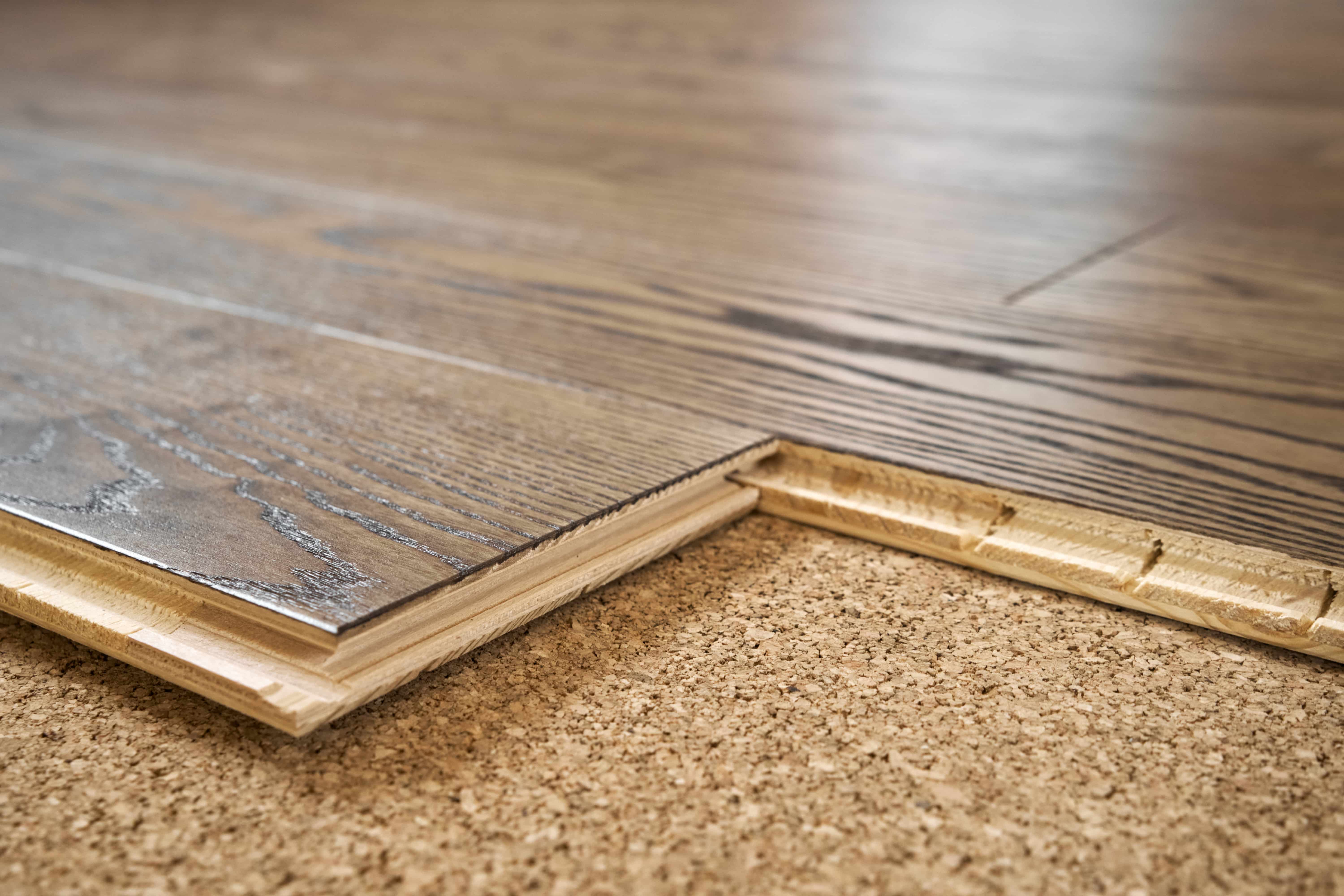The side profile of engineered hardwood is seen on a floor. The engineered hardwood has a dark finish and is placed over a cork underlay.