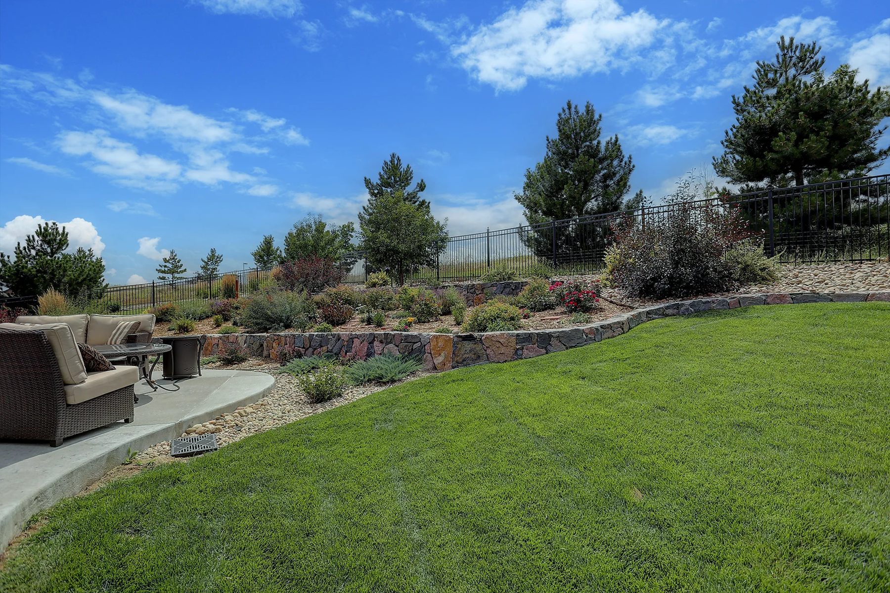 Backyard with a low stone wall, drought-tolerant planting, lawn and a patio with seating