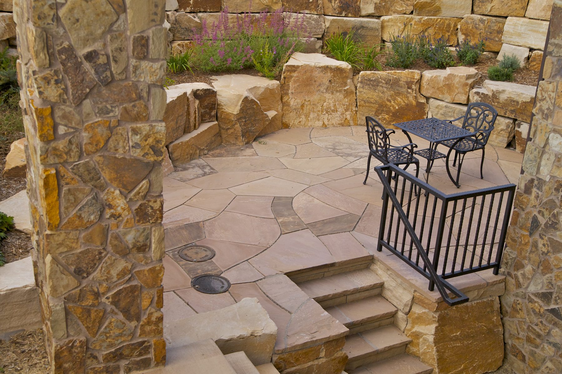 Irregular flagstone patio with stone steps, boulder retaining wall, and a small bistro table