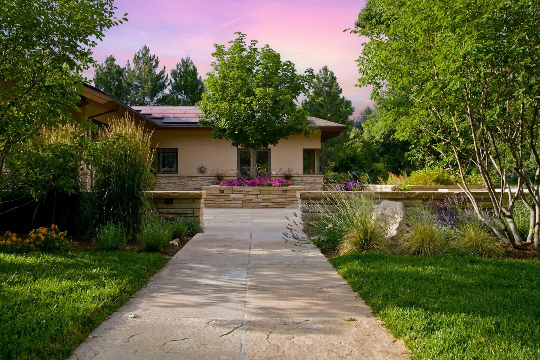 Finished stone entry walk with low stone walls, ornamental grasses and layered planting at dusk