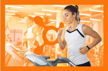 Woman running on treadmill in gym with blurred people and orange overlay with Orangetheory Fitness logo.