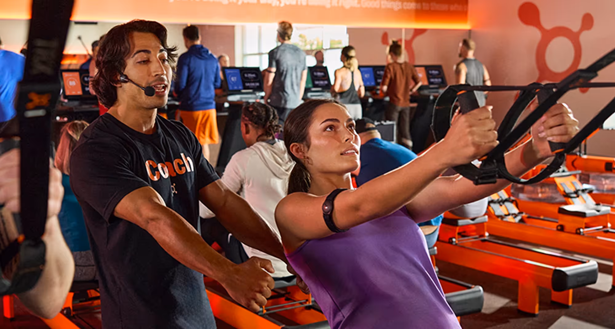  Fitness coach guiding a woman exercising with resistance bands in a gym with treadmills in the background.