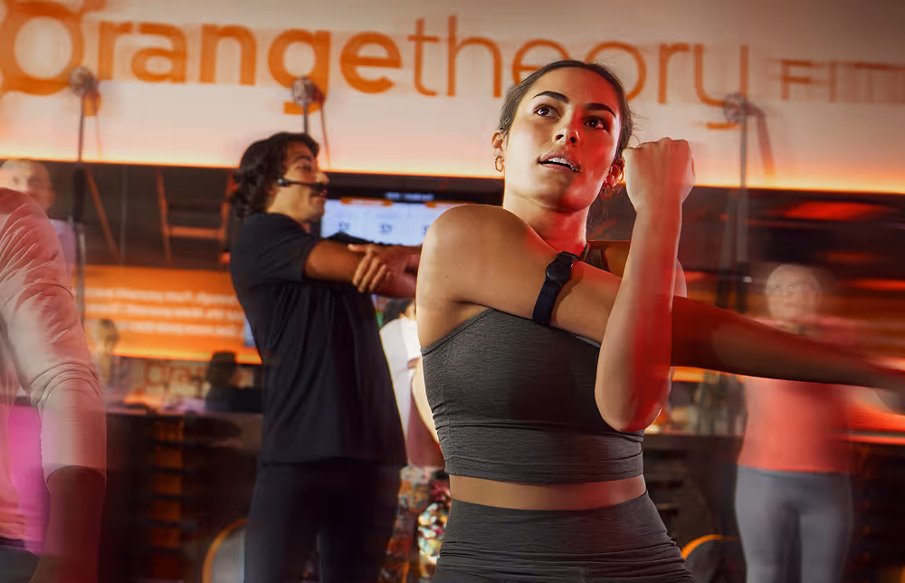 Woman in gray sportswear stretching her arm during a group fitness class at Orangetheory Fitness studio.