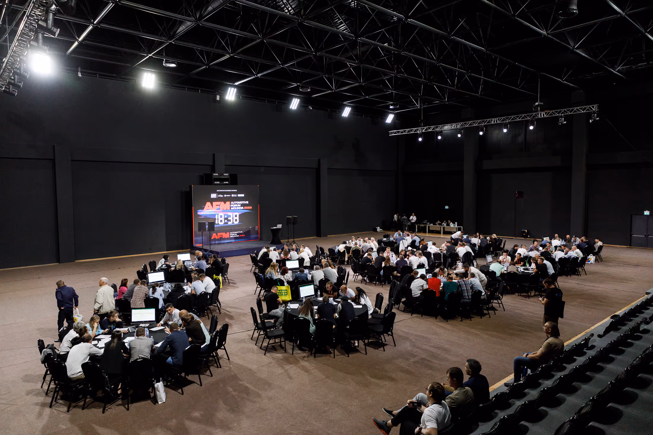 Большой зал с группами людей, сидящими за столами, на фоне экрана с надписью Automotive Forum Moldova 2023.
