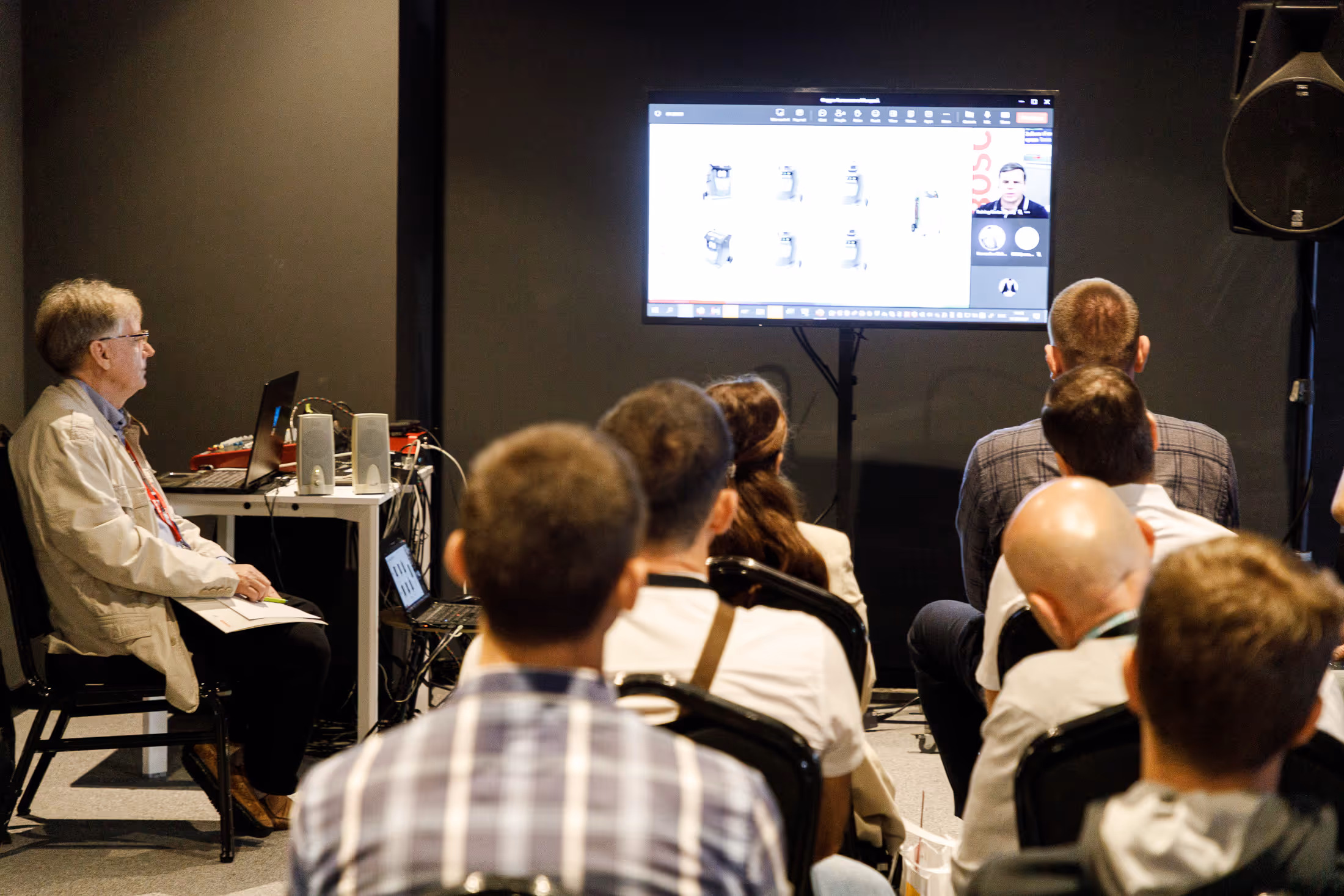 Группа людей сидит в зале, смотря на экран с презентацией и участником видеозвонка.