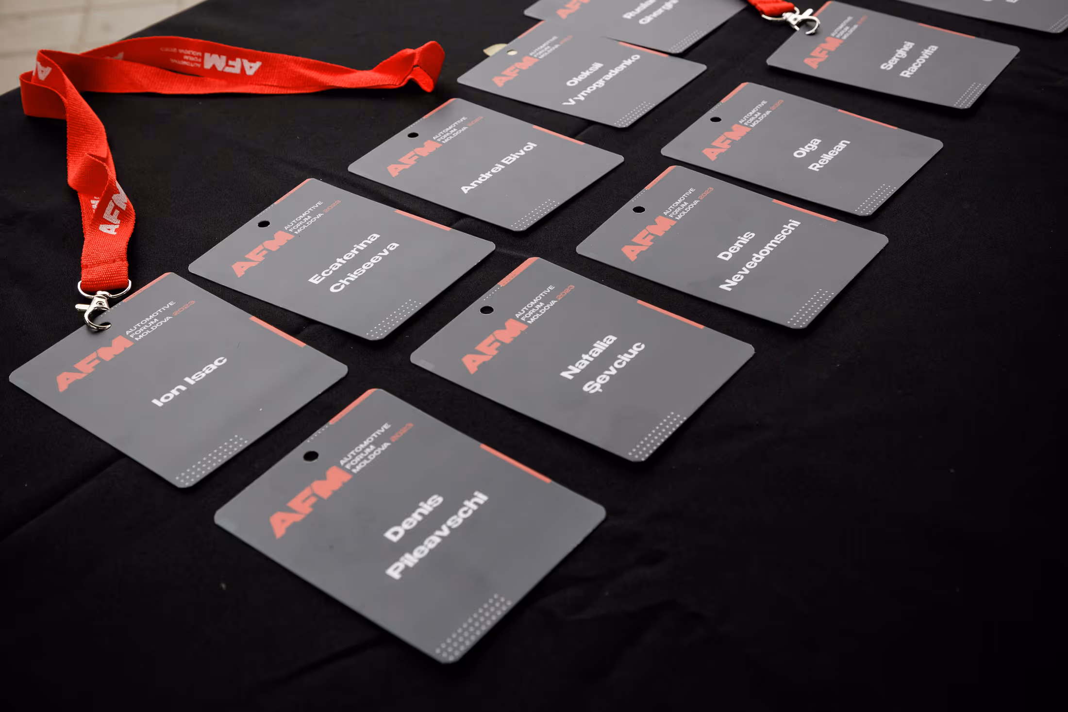 Именные бейджи Automotive Forum Moldova 2023 на черной поверхности, некоторые с красными шнурками.