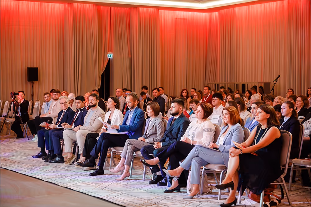 Аудитория, состоящая из мужчин и женщин в деловой одежде, сидящая в ряду на конференции.