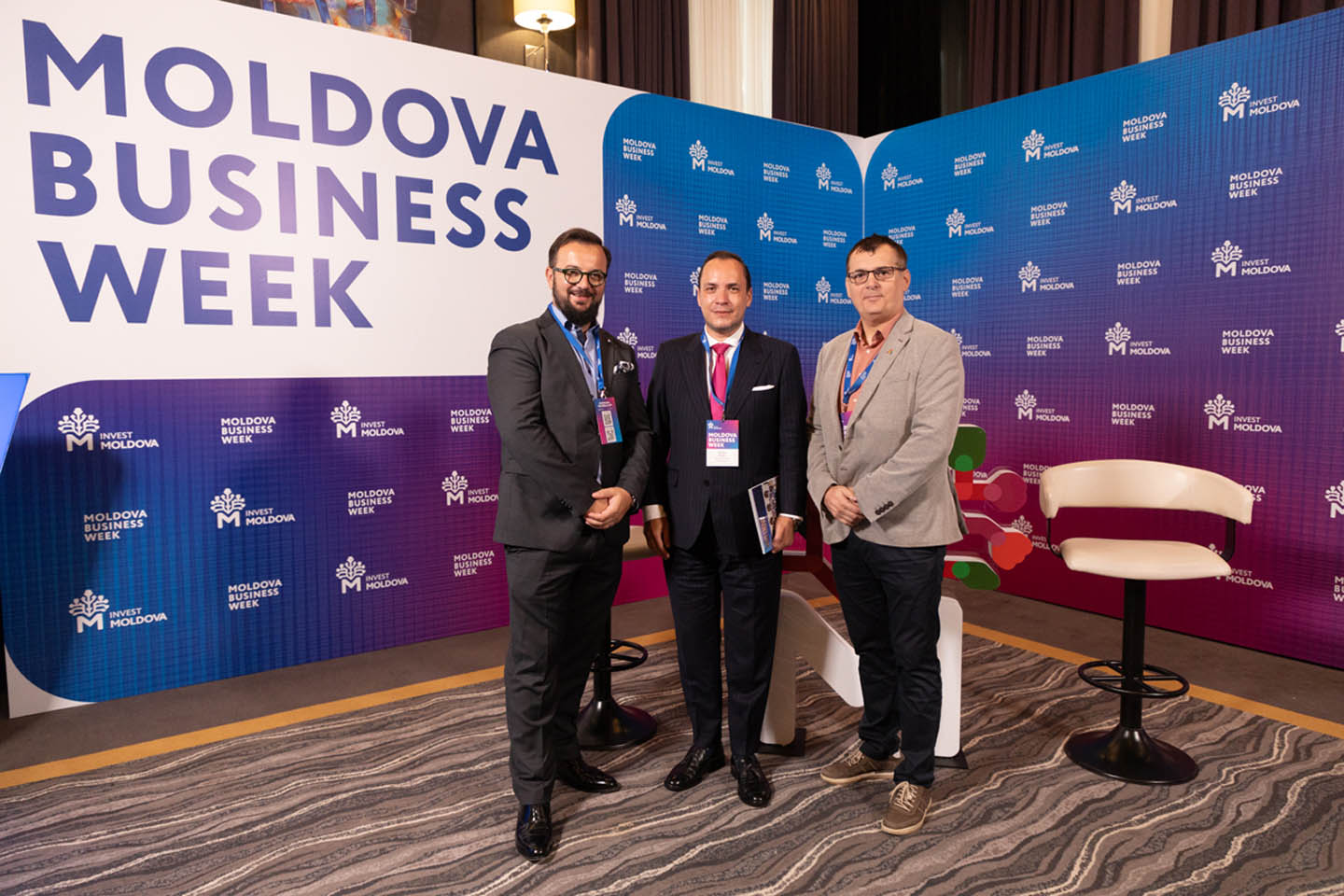 Три мужчины в деловой одежде позируют перед баннером с надписью Moldova Business Week.
