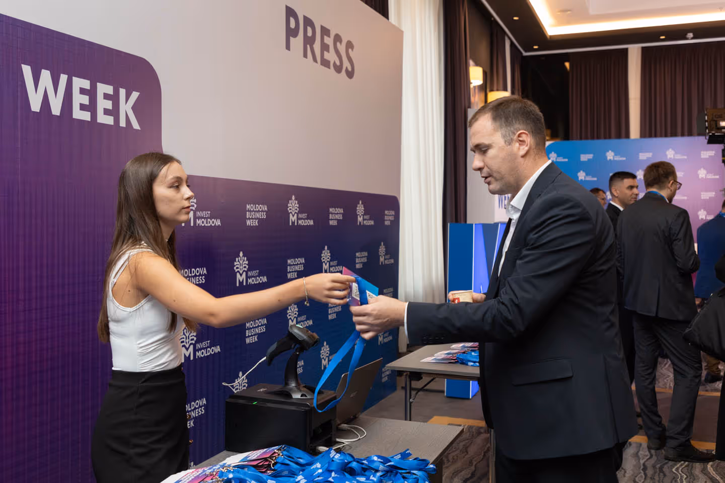 Женщина вручает бейдж мужчине в деловом костюме на мероприятии Moldova Business Week.