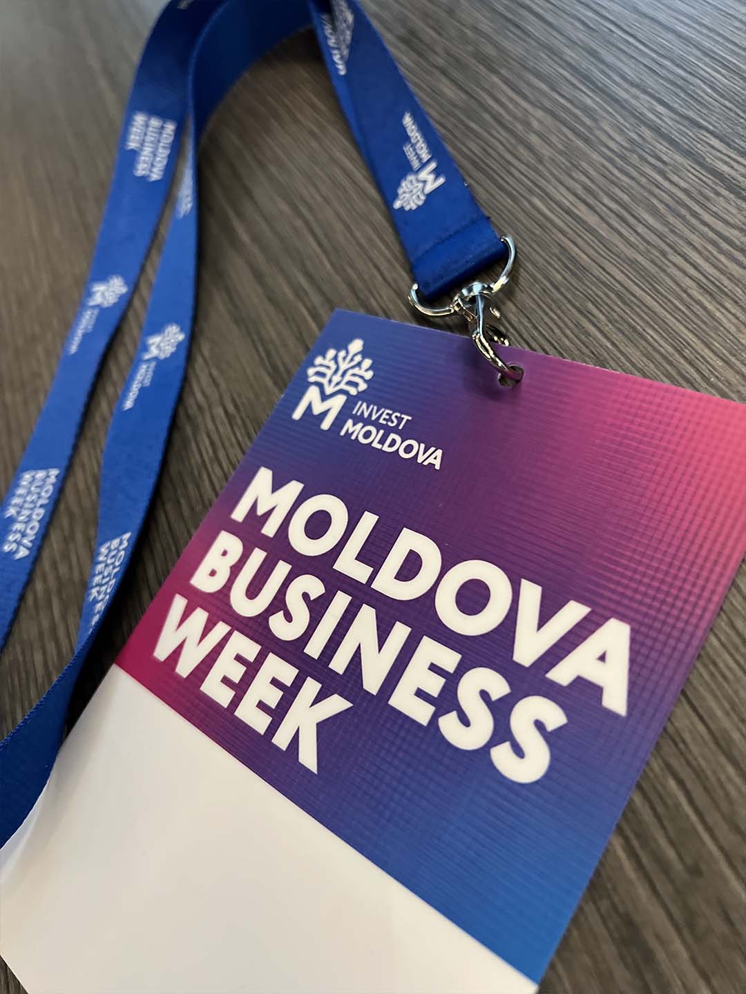 Бейдж и синий шнурок с надписью Moldova Business Week и логотипом Invest Moldova на деревянном столе.