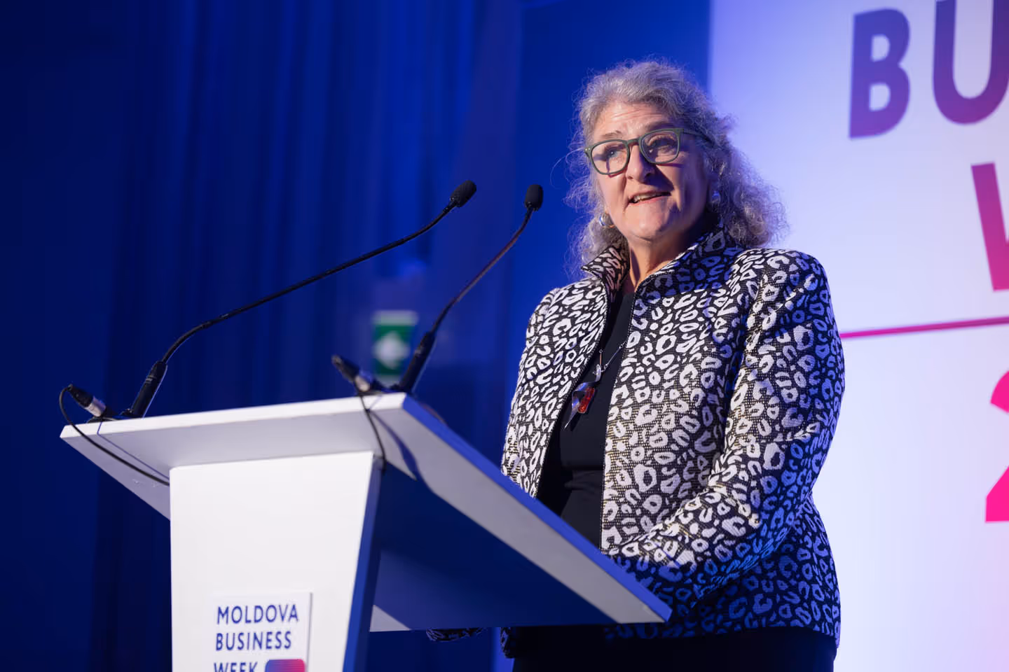 Женщина в очках и жакете с леопардовым принтом выступает за трибуной на мероприятии Moldova Business Week.