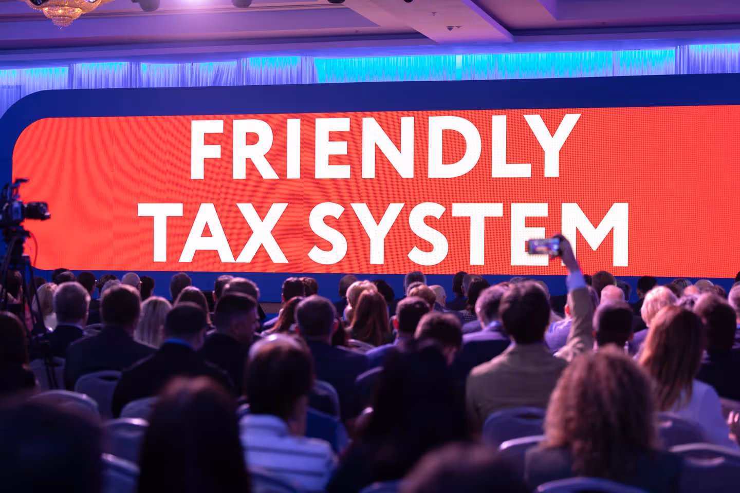 Аудитория слушателей на конференции с большим экраном, на котором надпись «Friendly Tax System».