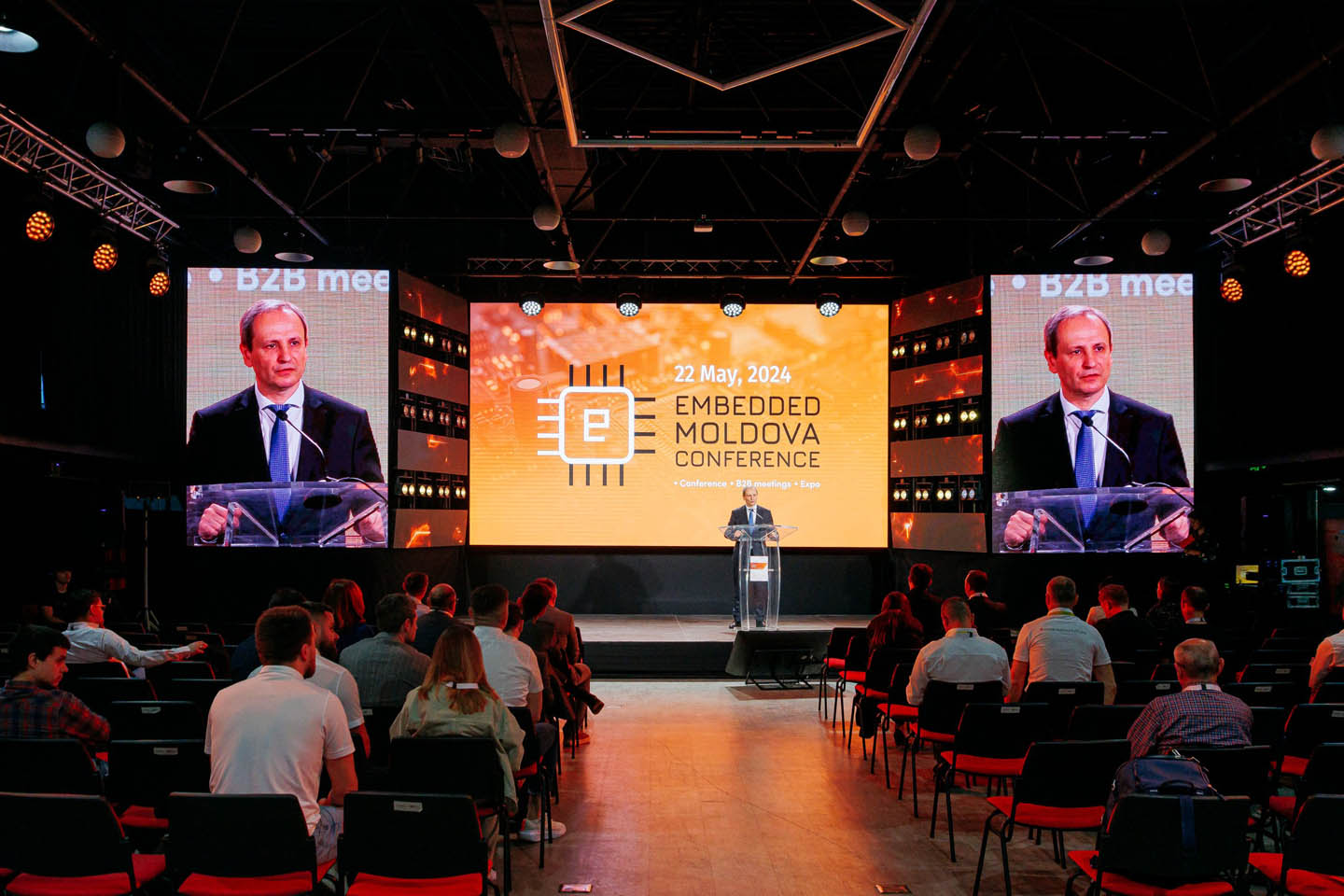 Спикер выступает на конференции Embedded Moldova 2024, аудитория слушает на фоне большого экрана с логотипом и датой.