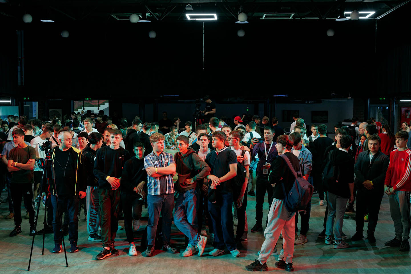 Группа молодых людей, стоящих в помещении, общающихся и ждущих начала мероприятия.