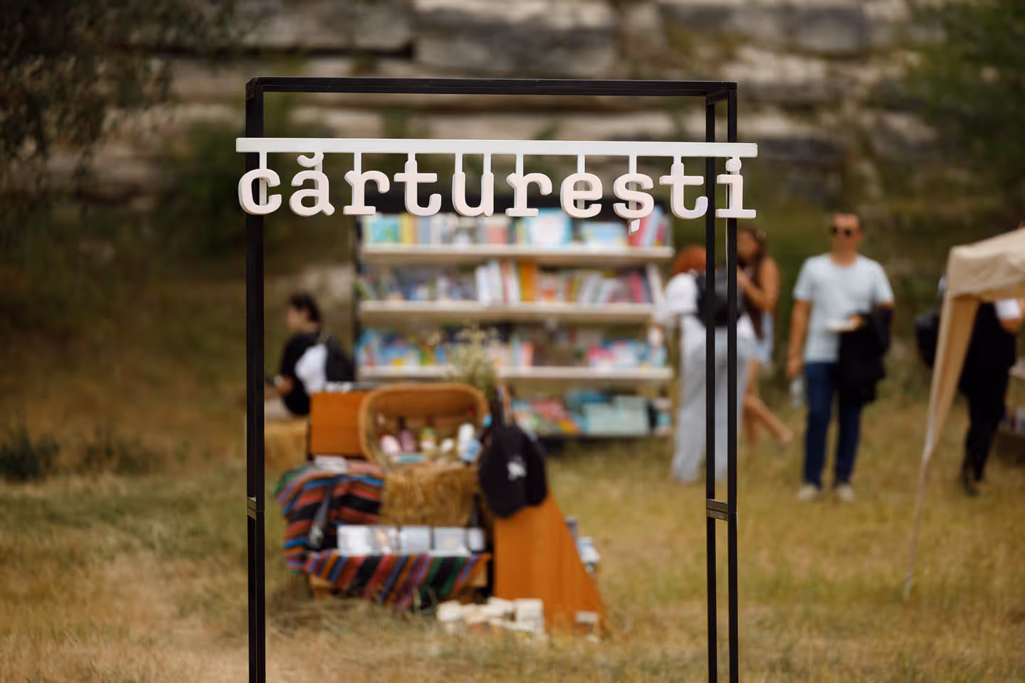 Вывеска с надписью «Cărturești» на черной металлической раме на фоне размытых книжных полок и людей на открытом воздухе.