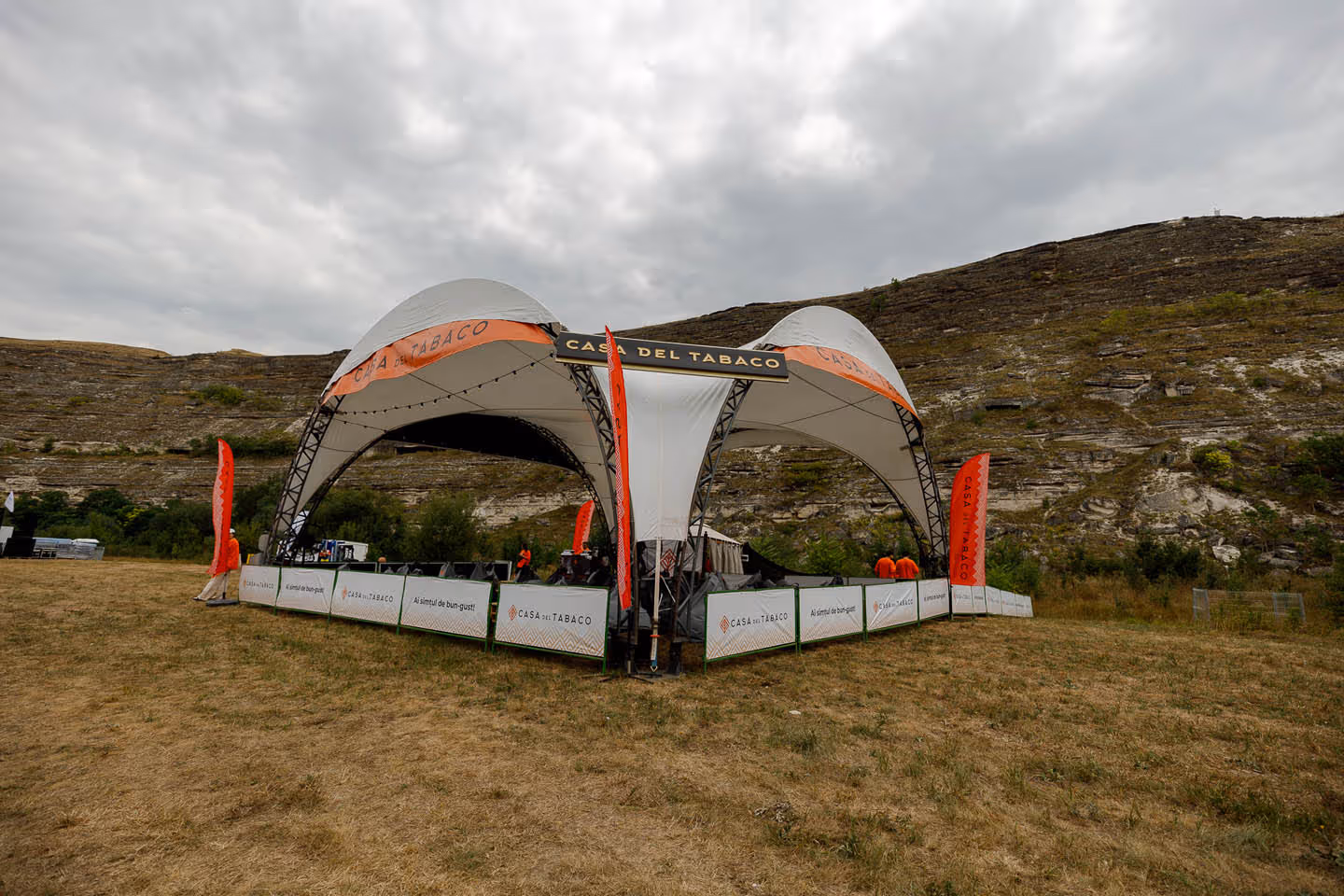 Белая шатровая сцена с надписью Casa del Tabaco на фоне холмов под облачным небом.