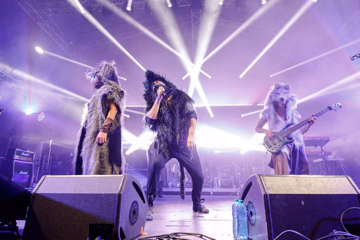 Исполнители на сцене в костюмах с искусственным мехом, освещённые яркими прожекторами во время концерта.