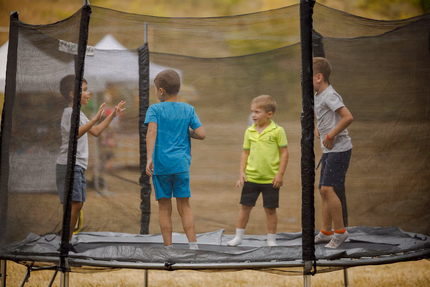 Четверо детей играют на батуте с защитной сеткой на открытом воздухе.