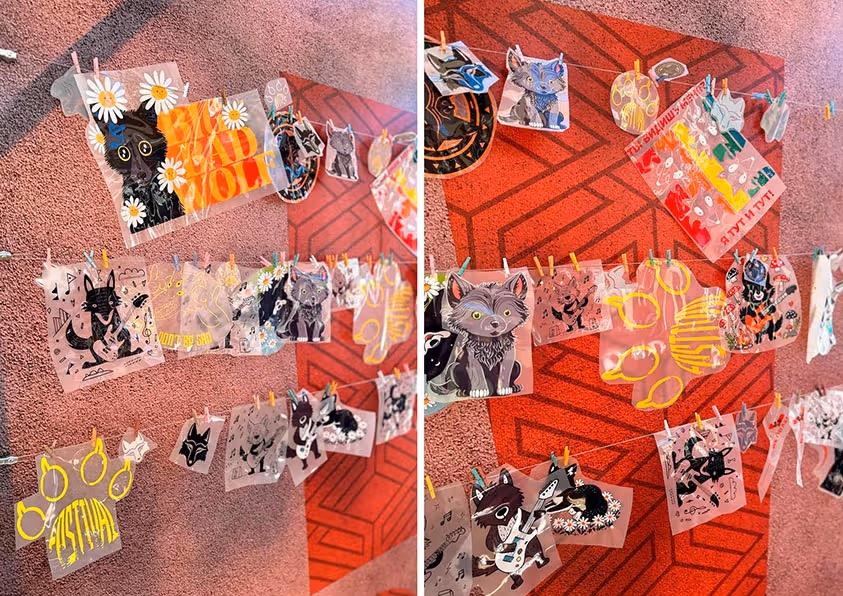 Несколько цветных иллюстраций с изображением волков и надписями, прикрепленные прищепками к красной стене с узором следа лапы.