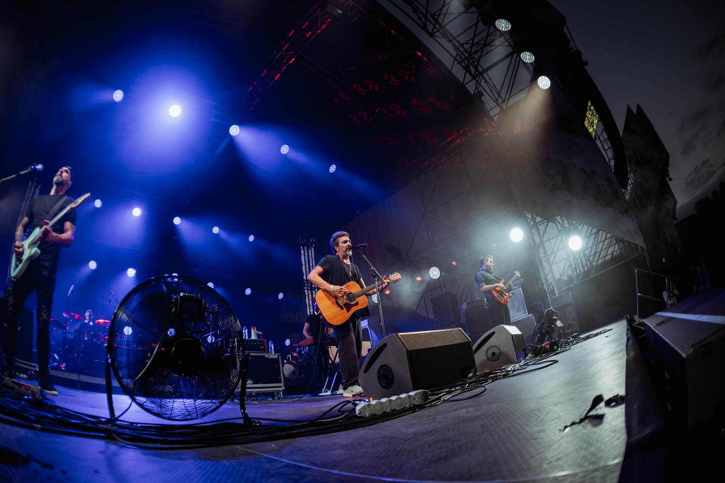 Группа музыкантов на сцене под синими и белыми прожекторами во время ночного концерта.