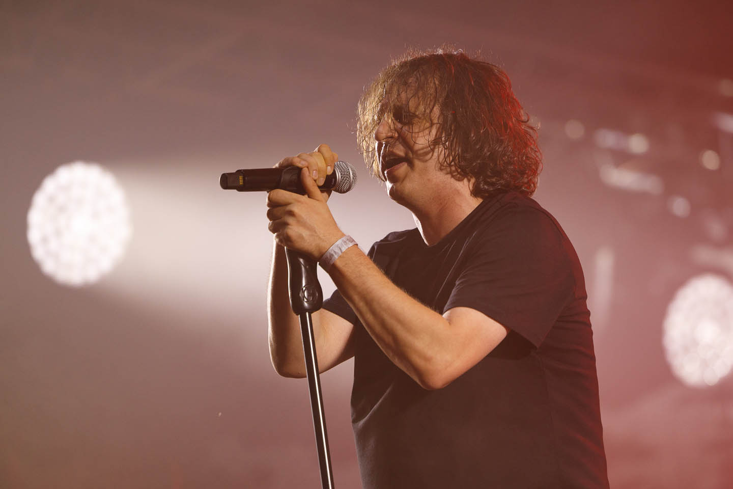Мужчина с каштановыми волосами поет в микрофон на сцене с ярким освещением.