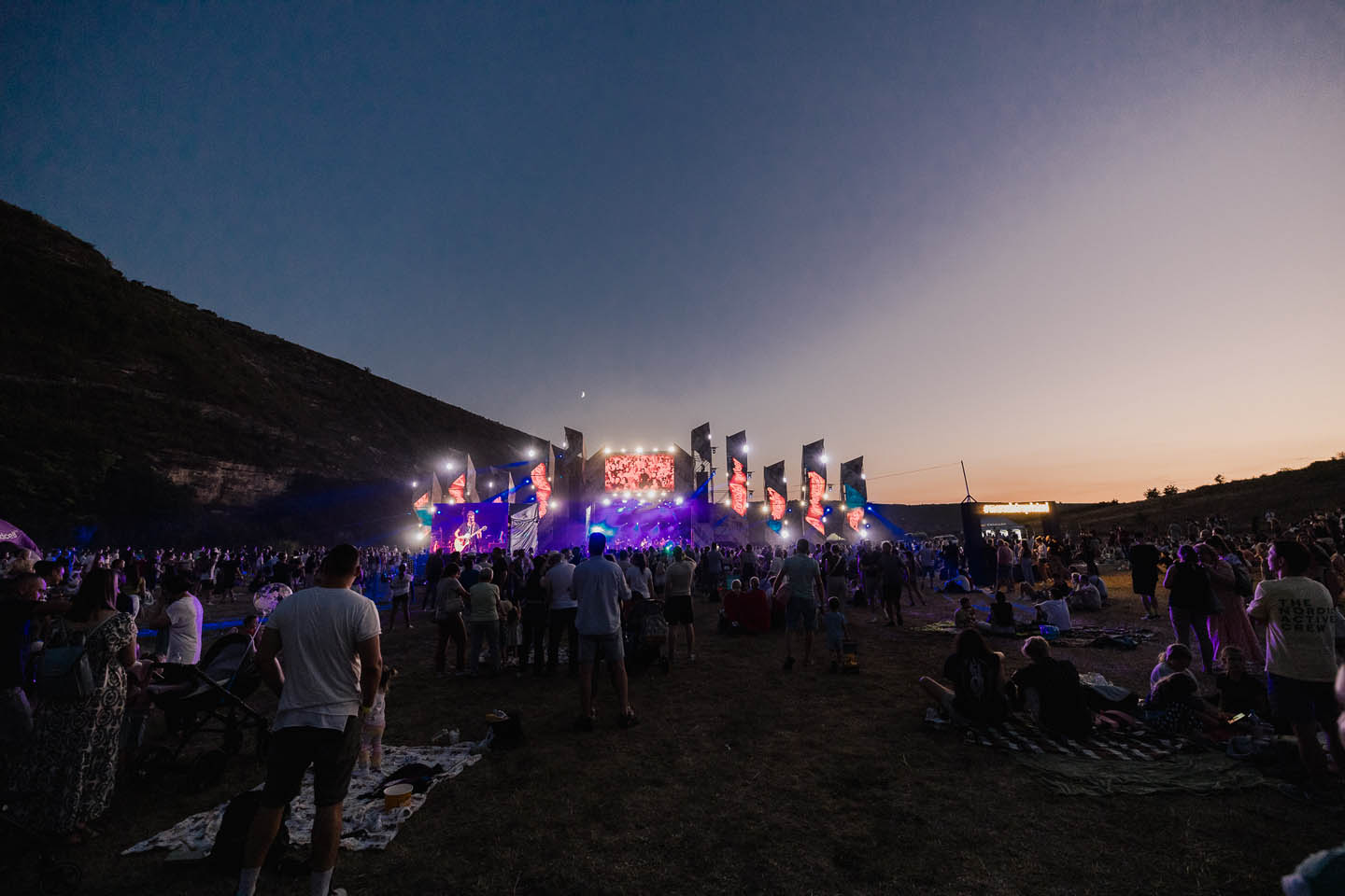 Вечерний музыкальный фестиваль на открытом воздухе в долине с большой сценой и зрителями.