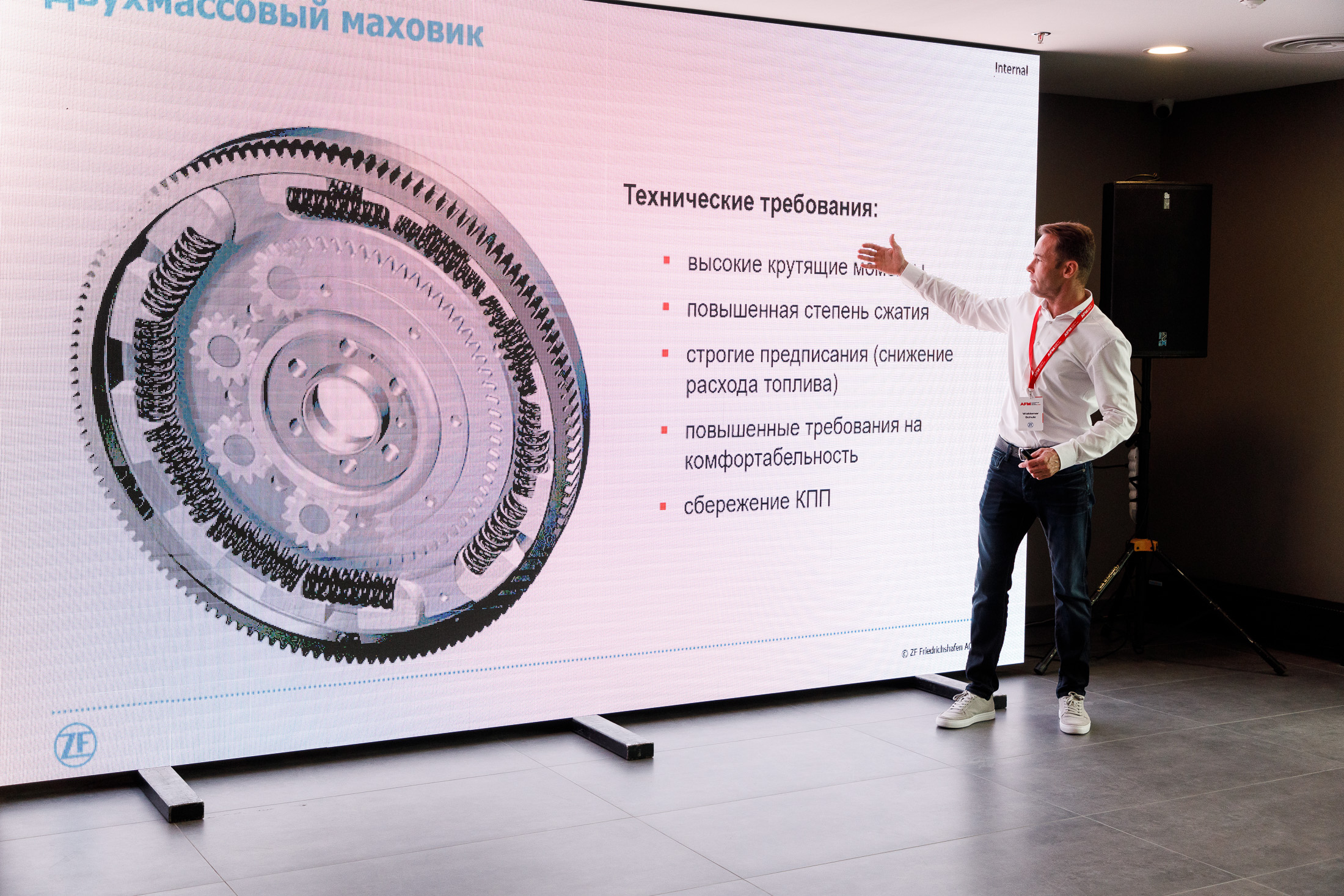 Мужчина показывает на технические требования и изображение двухмассового маховика на большом экране.