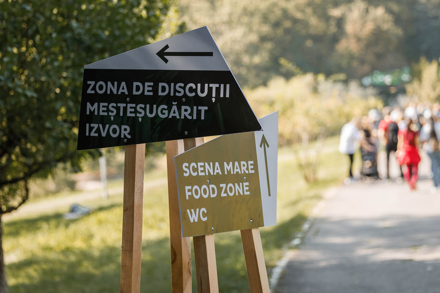 Информационные таблички на деревянных стойках у тропинки в парке с указателями к зоне обсуждений и зоне еды.