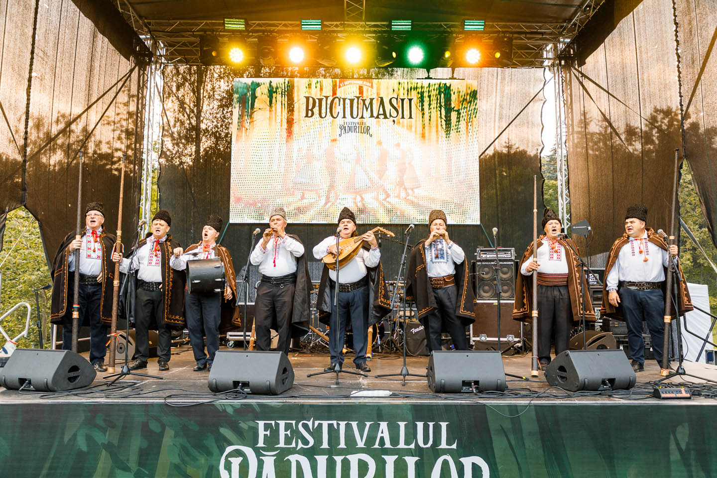 Группа мужчин в традиционной одежде выступает на сцене фестиваля с народными музыкальными инструментами.