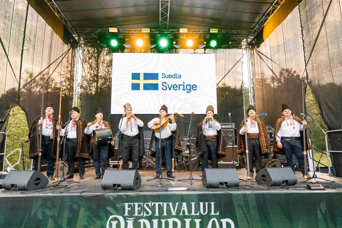 Группа мужчин в традиционных костюмах выступает на сцене под светом софитов на фестивале.