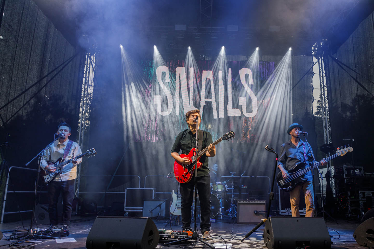 Музыкальная группа Snaаils выступает на сцене с гитарами и микрофонами под освещением прожекторов.