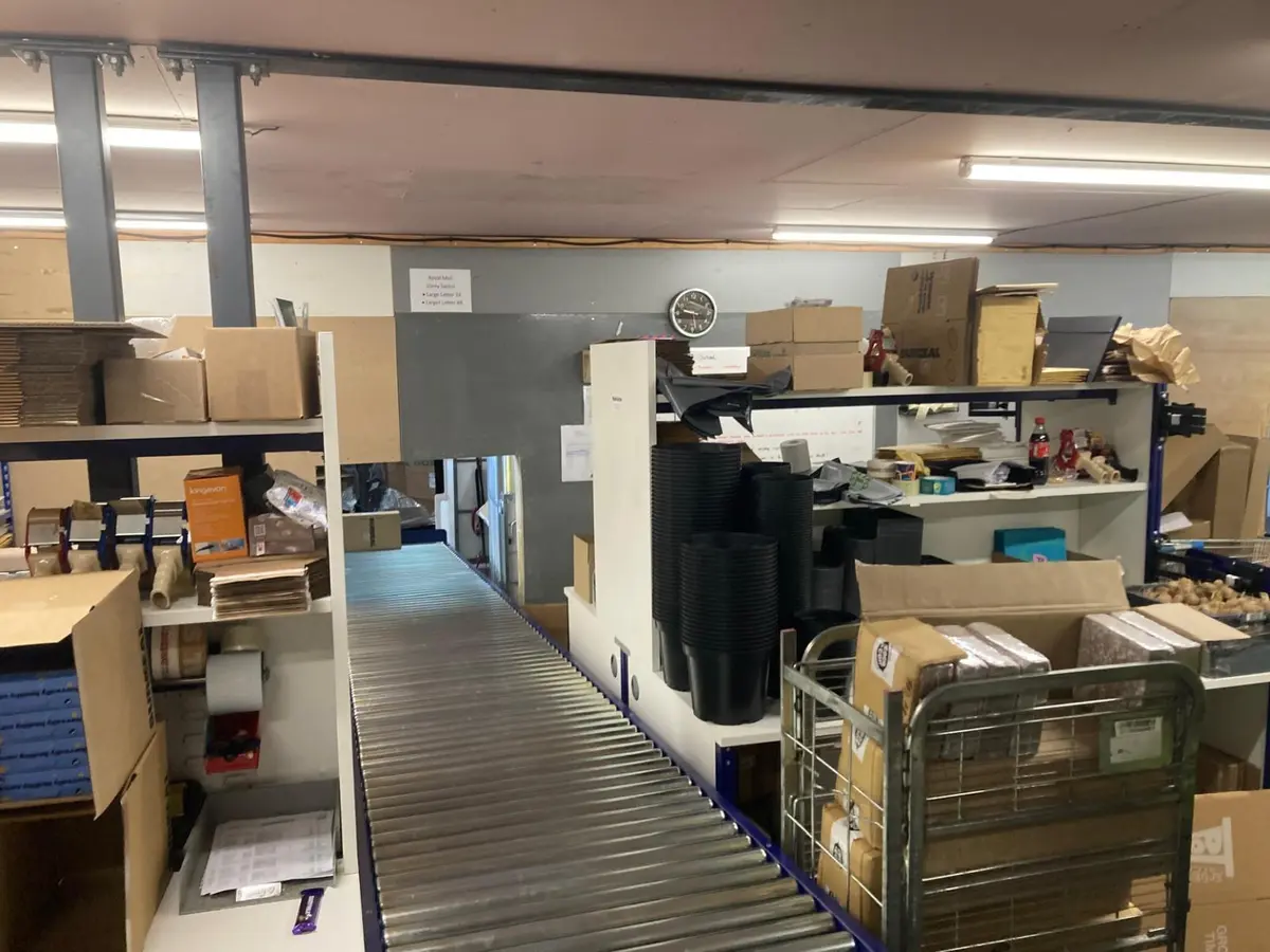 Pack bench with integrated roller conveyor and organised packaging storage