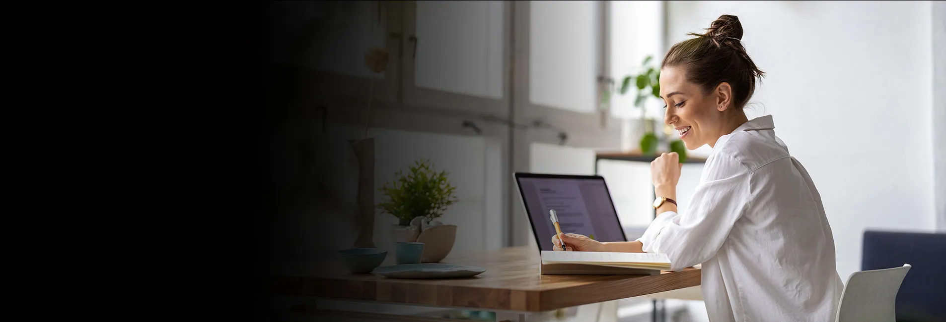 woman sitting at her desk working on her laptop and writing notes