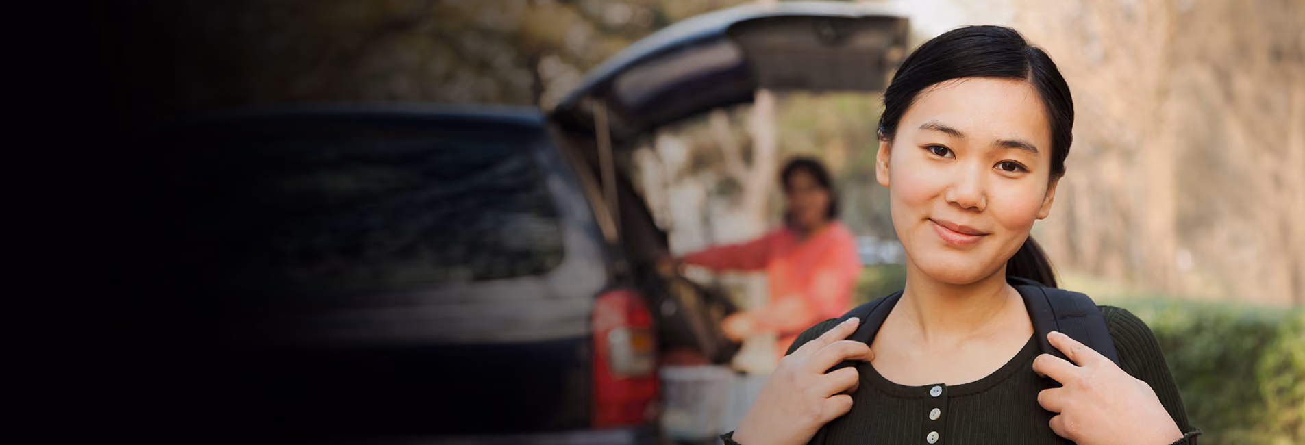 College student on move in day with her mom in the background unloading the car.