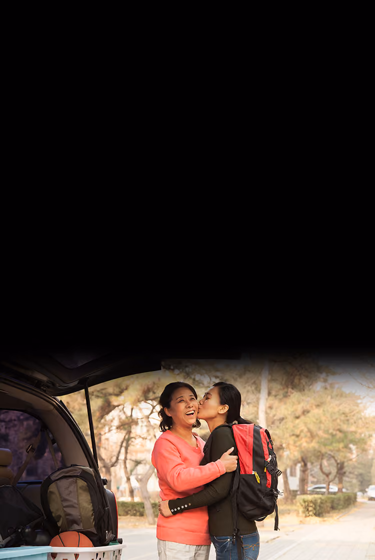Young woman hugs mom while standing by car loaded up for move to college.
