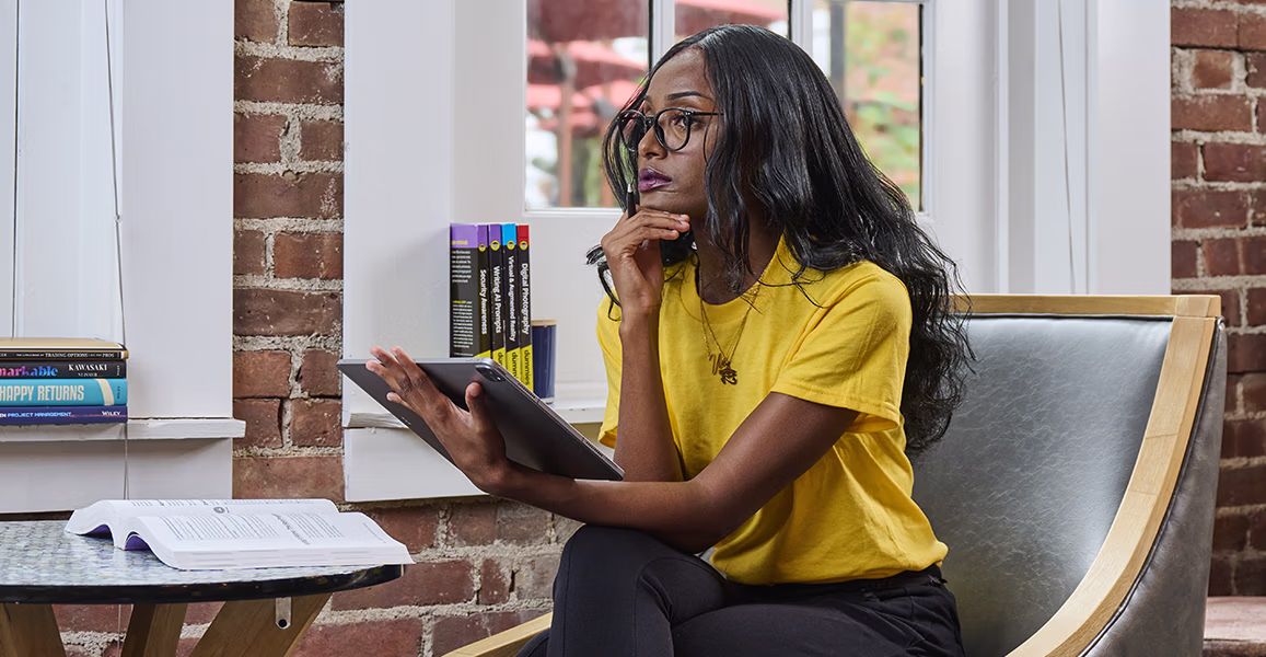 woman looking at tablet with for dummies book on table in front of her with more books on bookshelf behind her