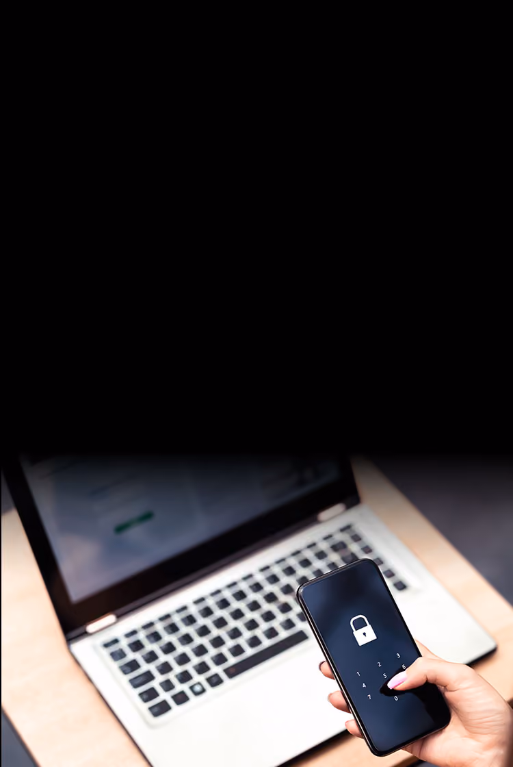 person holding locked phone with laptop in background