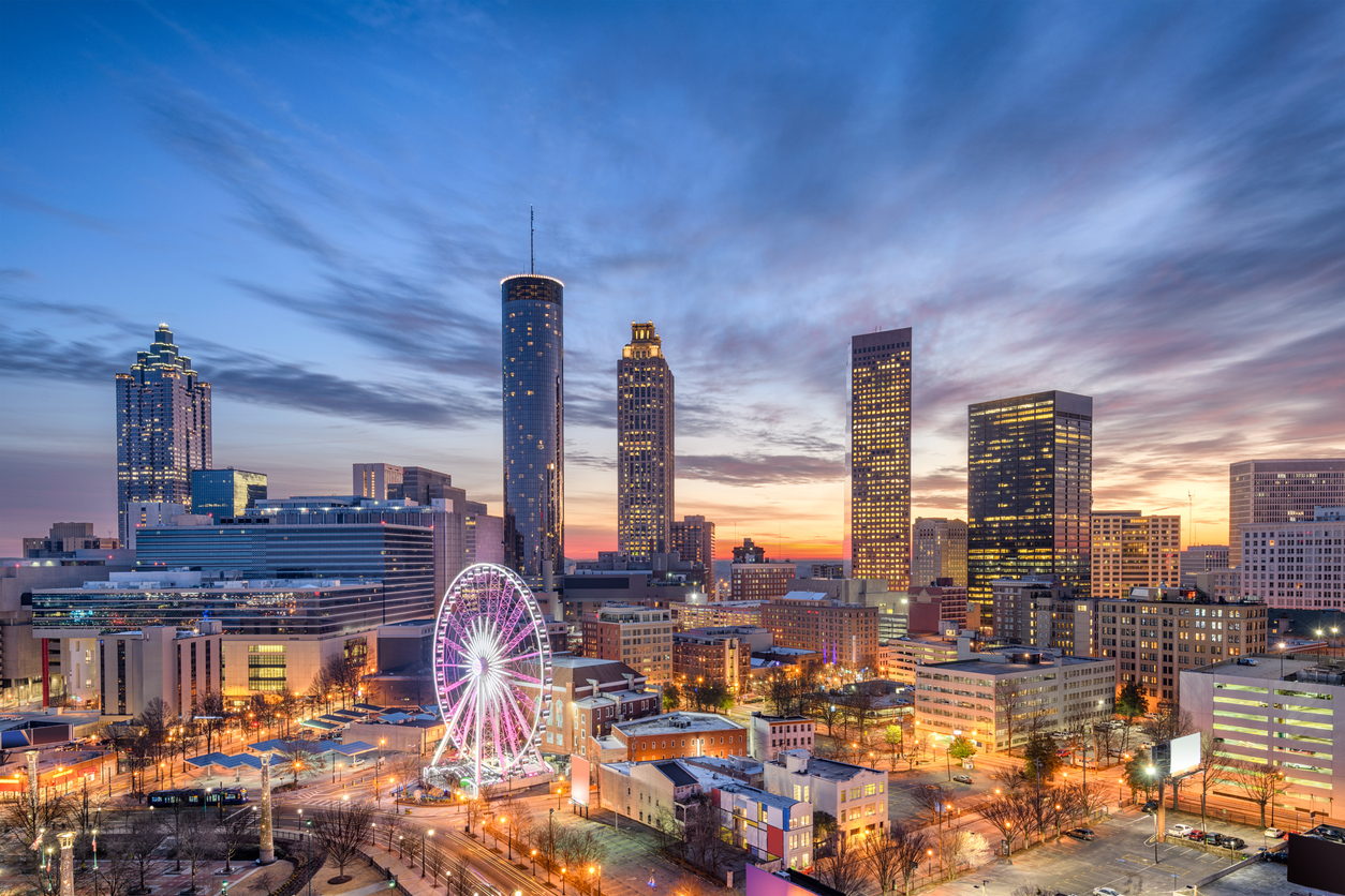 Atlanta city skyline at sunset with illuminated Ferris wheel and tall buildings under a vibrant blue and orange sky.