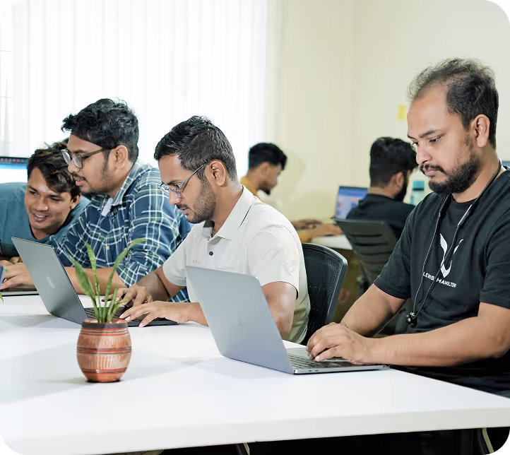 A group of men sitting around a table working on laptops.