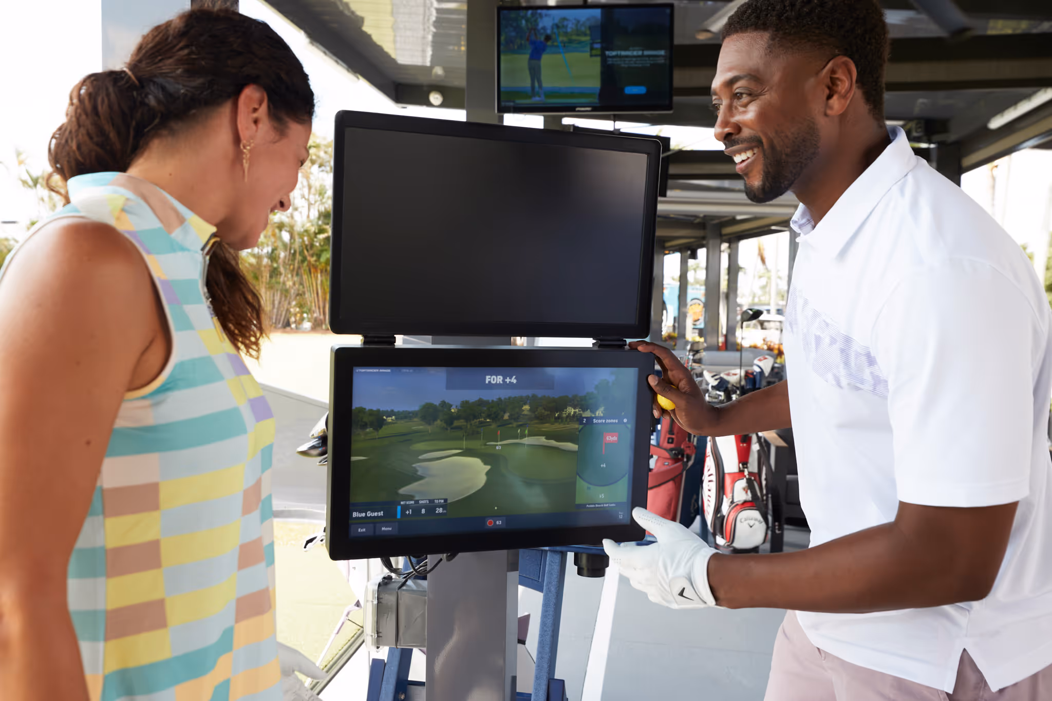 Two golfers looking at a digital screen displaying golf course data and scores at a golf driving range.