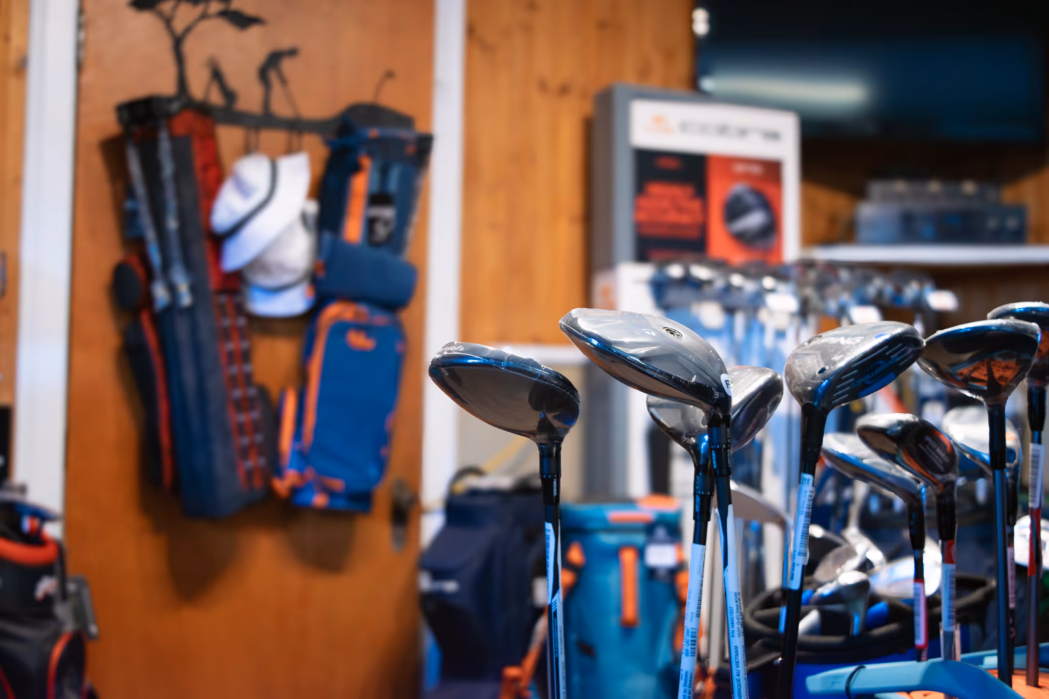 Close-up of new golf club drivers on display in the Archie's pro shop with golf bags and accessories in the background.