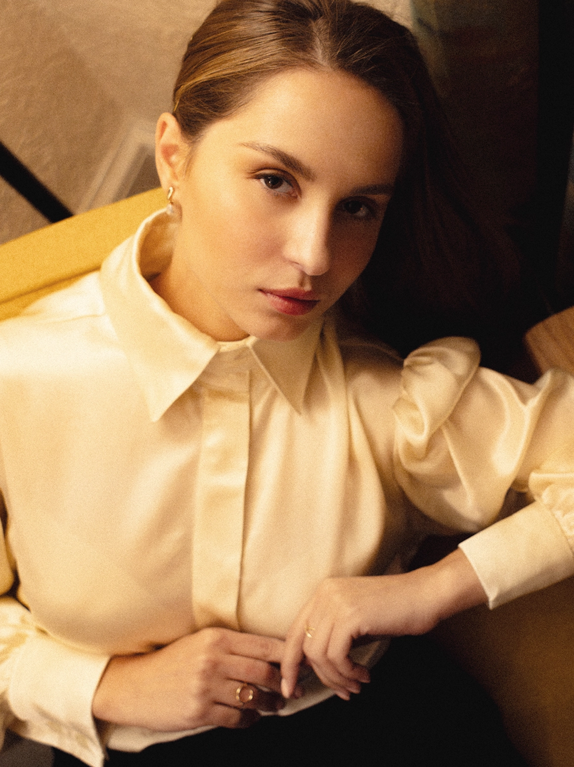 A women in a chair posing wearing a satin crepe silk blouse.