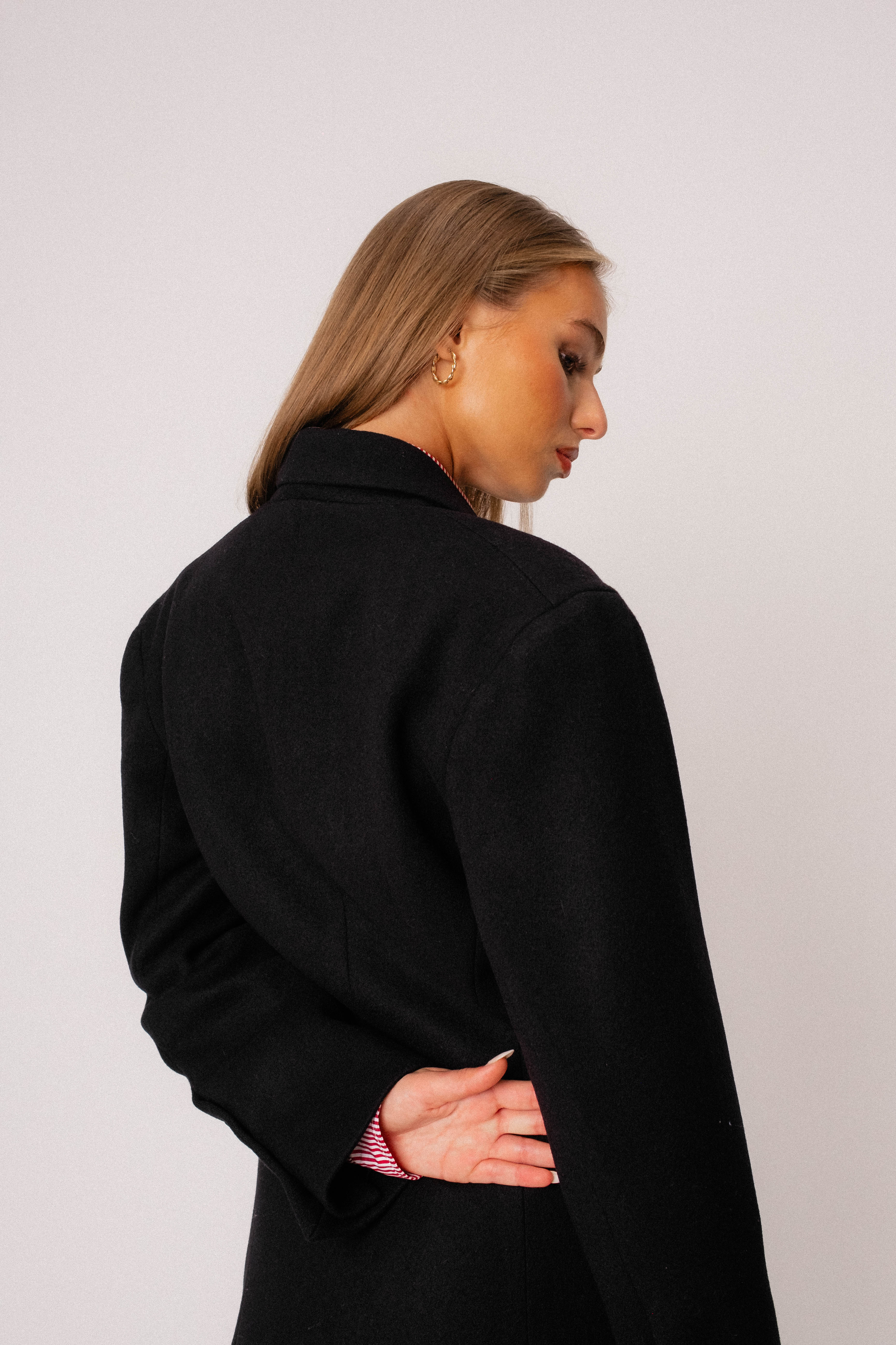 The back of a wool womens coat worn by a model in a studio.