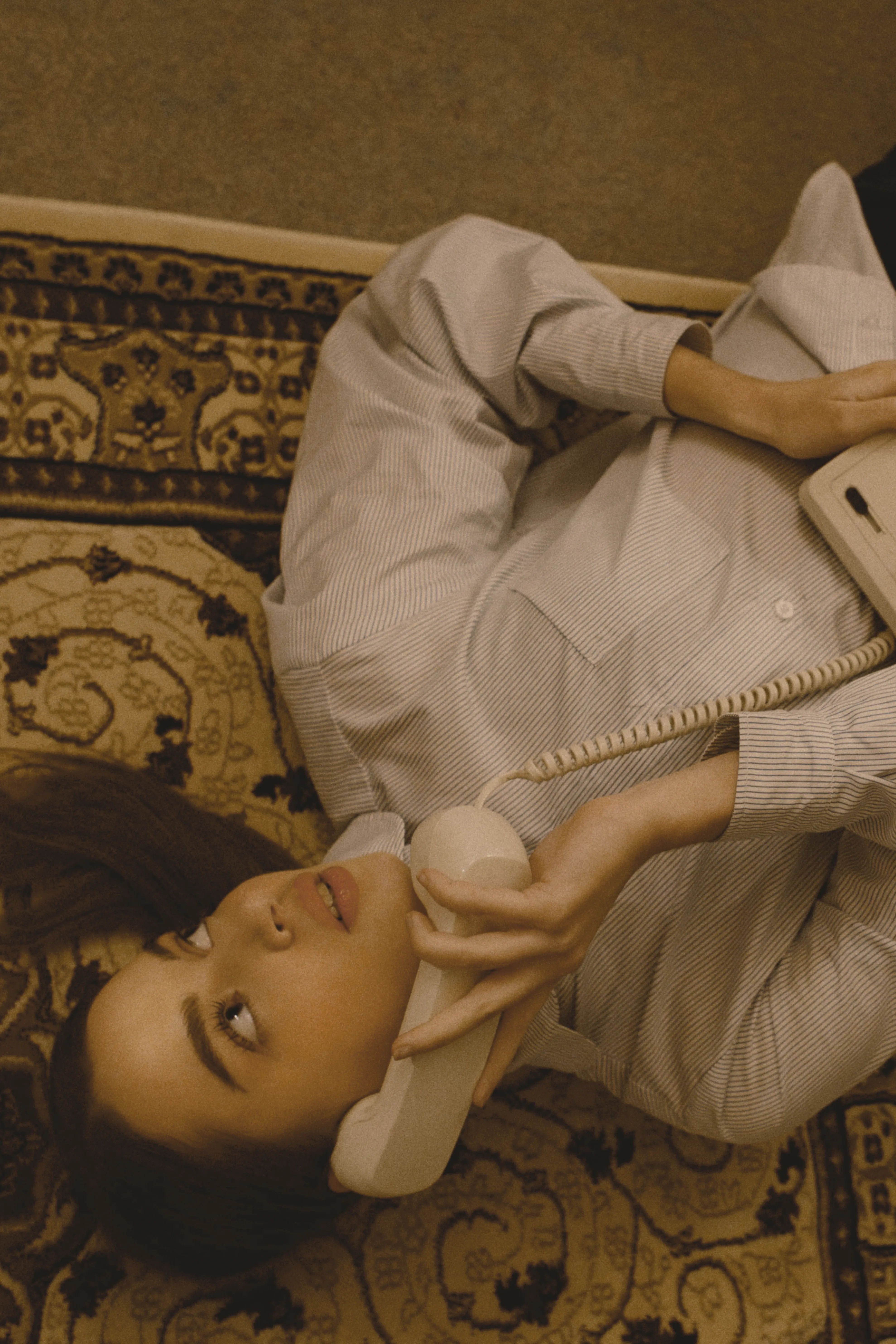 A women on the phone laid on a rug in stripped cotton womens shirt talking on the phone.
