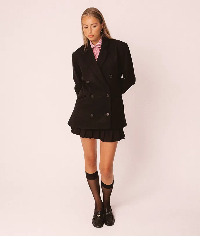 A women in a studio wearing a wool, black double breasted coat wearing a striped cotton shirt.